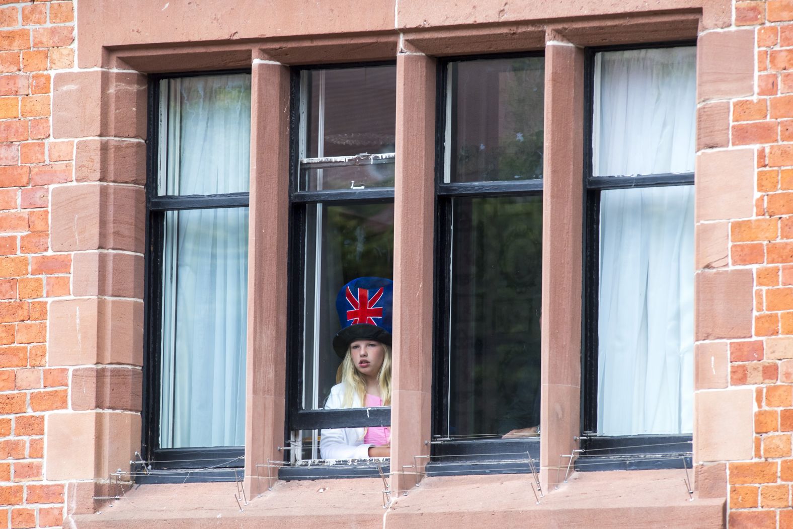 A girl looks out a window awaiting an appearance of Meghan and the Queen.
