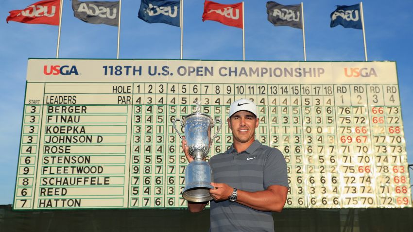 SOUTHAMPTON, NY - JUNE 17:  Brooks Koepka of the United States celebrates with the U.S. Open Championship trophy in front of the final leaderboard after winning the 2018 U.S. Open at Shinnecock Hills Golf Club on June 17, 2018 in Southampton, New York.  (Photo by Andrew Redington/Getty Images)