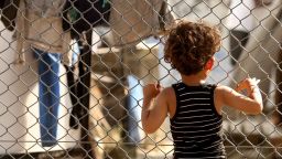 MYTILENE, GREECE - MAY 20:  A refugee child looks through a fence at the Moria refugee camp on May 20, 2018 in Mytilene, Greece. Despite being built to hold only 2,500 people, the camp on the Greek island of Lesbos is home to over 6,000 asylum seekers who crossed the Aegean Sea from Turkey's nearby shore by boat, usually at night to avoid interception. Although the numbers of arrivals are lower than at the beginning of the crisis in 2015, when Syrians and Iraqis fled ISIS-controlled strongholds, boatloads of refugees from those countries and other troubled areas continue to land there, and critics say the local governments have yet to manage the situation, leading the squalid conditions at Moria to be seen as symbolic of poorly-managed policy. The camp, on the site of a former military base, is comprised of shipping containers, tents, and improvised shelters of wooden pallets and tarps, whose residents stranded there complain of poor food, power failures, disease, lack of medical care, and poisonous snakes as they wait to obtain transfer to the mainland and less temporary legal status.  (Photo by Adam Berry/Getty Images)