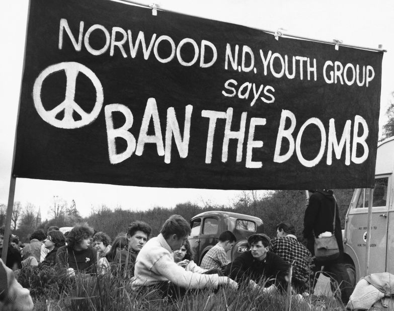 A group of anti-nuclear weapons protesters sit beneath a "ban the bomb" banner at a protest.