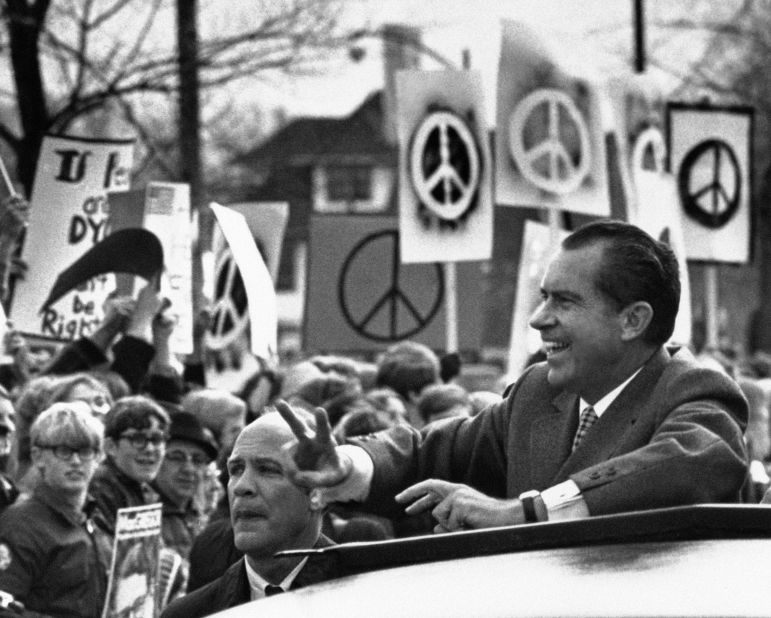 Surrounded by a sea of peace symbols, President Richard Nixon gives the "V" sign as his motorcade passes a group of demonstrators in Rochester, Minnesota in October 1970. 