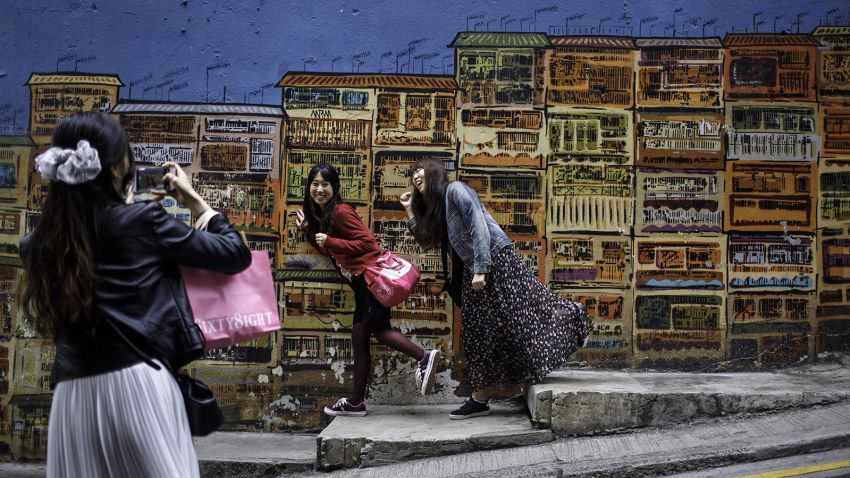 In this photo taken on March 11, 2017, Korean tourists pose for photographs in front of street art along Graham Street in Hong Kong's SoHo district.From graffiti shows to major installations, Hong Kong will see a creative surge as Art Basel comes to town this week, but residents want a more permanent change to the visual landscape. / AFP PHOTO / TENGKU Bahar / TO GO WITH AFP STORY: Hong Kong-art-culture-basel-lifestyle, FEATURE by Aaron TAM        (Photo credit should read TENGKU BAHAR/AFP/Getty Images)