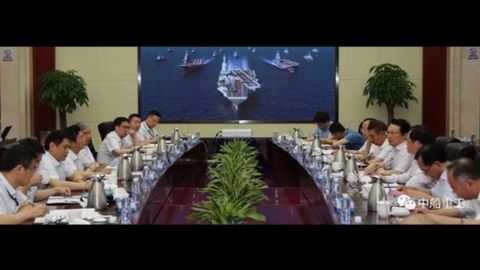 Screen shot from Chinese media shows a conference at the No.701 Research Institute of China Shipbuilding Industry Corporation with picture in the background of China's two current ski-jump carriers flanking a larger ship with a flat deck thought to picture what China's third aircraft carrier will look like.