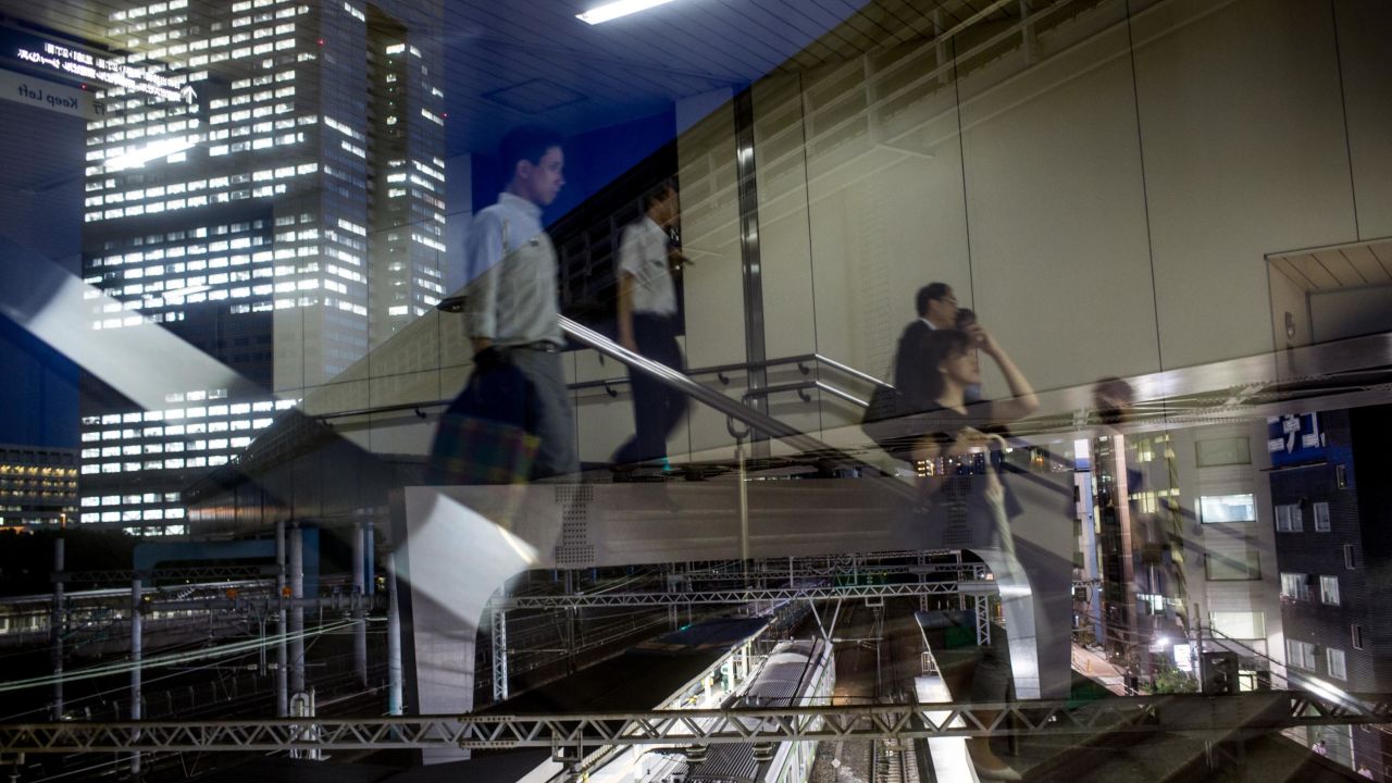 Office workers are seen reflected in a window as they walk to a train station in Tokyo. Japan's intense work culture has been criticized for being too harsh on employees. 