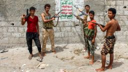 Yemeni fighters from the Amalqa ("Giants") Brigades loyal to the Saudi-backed government stand pointing their Kalashnikov assault rifles towards a Huthi-rebel banner painted on a wall, reading in Arabic "God is the greatest... Death to America, death to Israel, cursed be the Jews, victory for Islam", on the southern outskirts of the Red Sea port city of Hodeida near the airport on June 21, 2018. - The "Giant Brigades" are a former elite unit of the Yemeni army rebuilt by the UAE which has been at the vanguard of the offensive, reinforced by thousands of fighters from southern Yemen. (Photo by Saleh Al-OBEIDI / AFP)        (Photo credit should read SALEH AL-OBEIDI/AFP/Getty Images)