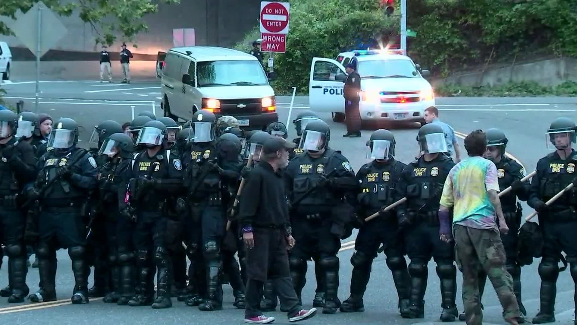 A couple protesters stand Thursday morning near officers in riot gear as they block an entrance to the Portland ICE facility.