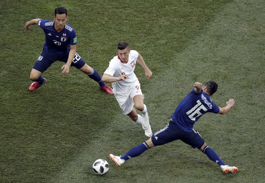 Poland forward Robert Lewandowski dribbles through two Japan players.