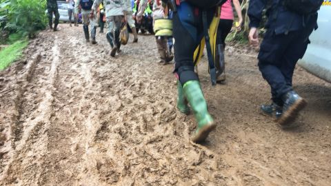 Rescue workers tramp through thick mud close to the entrance of the cave.