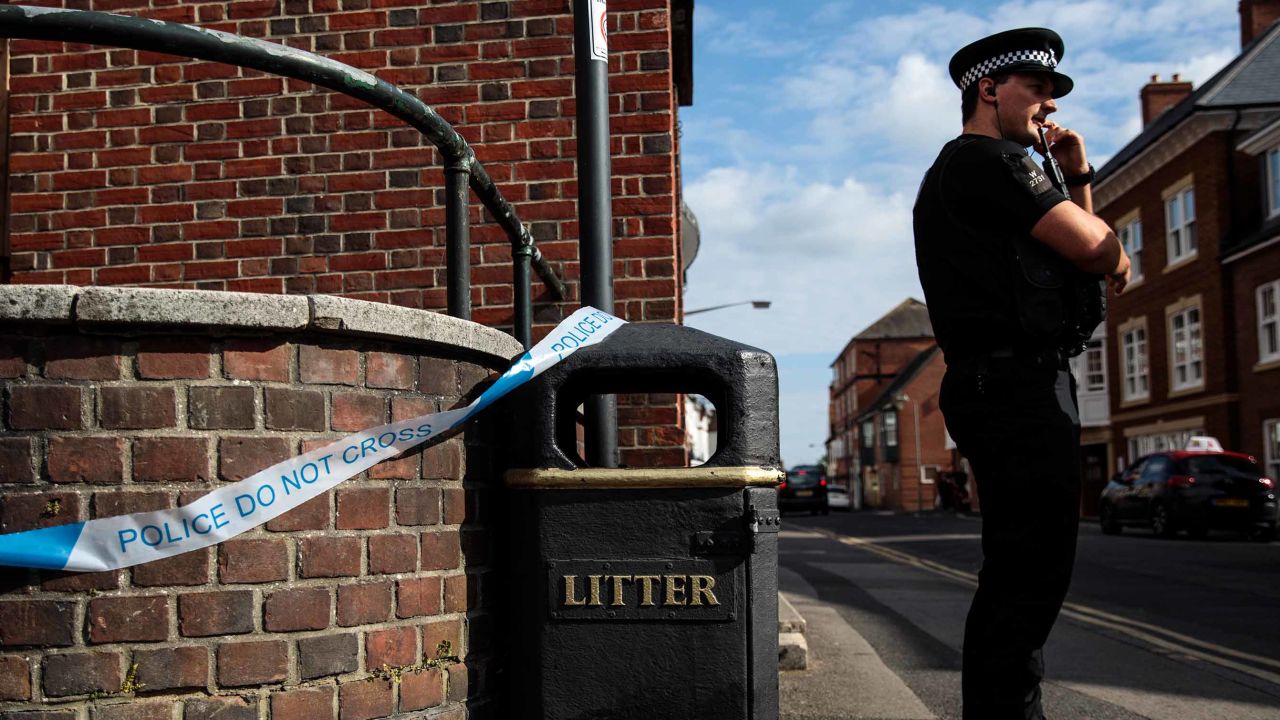 A police officer stands at a cordon around a public trash can Wednesday next to a supported housing project in Salisbury, thought to be connected to the Amesbury victims.