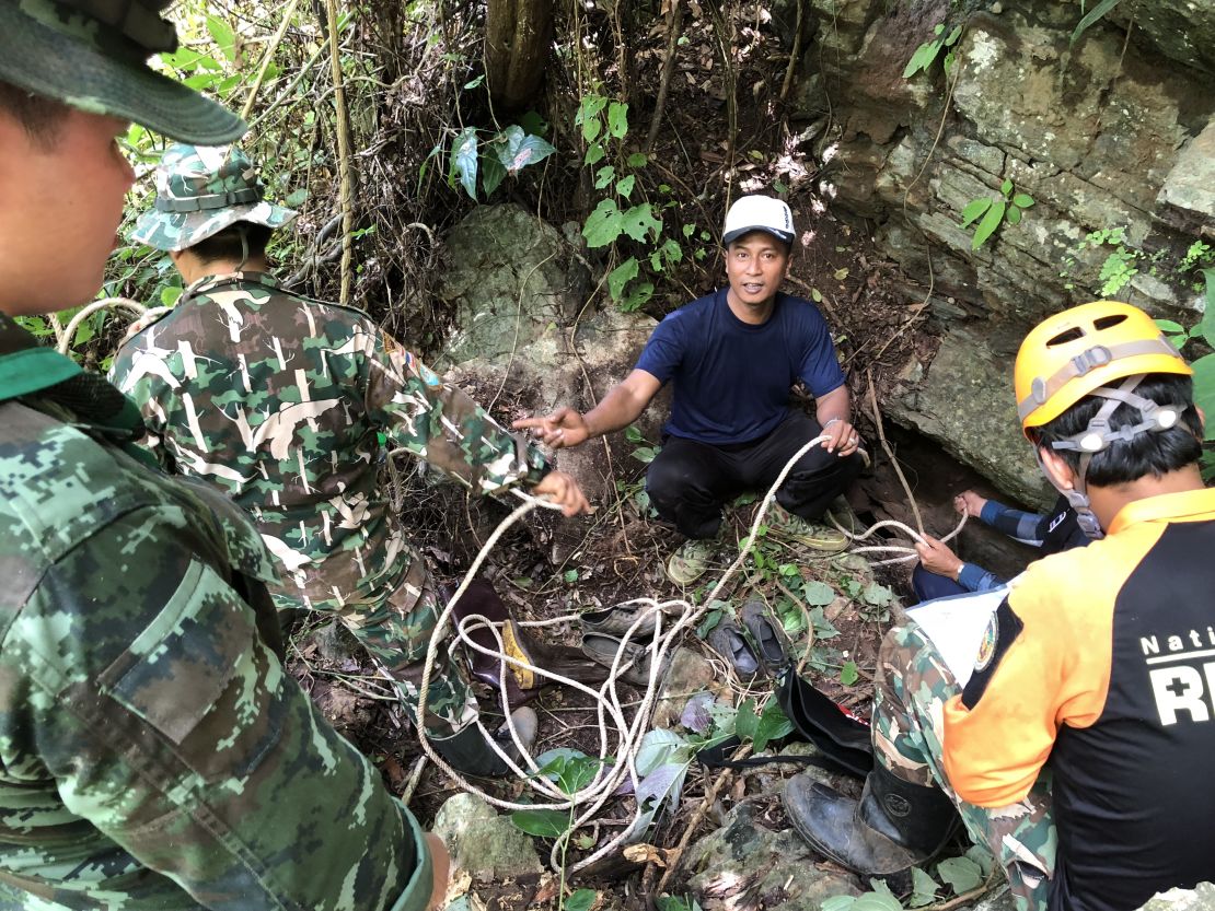 Expert mountaineering volunteers prepare to descend into an opening in the rock face to investigate if there is a route to the cave where the boys are. They are accompanied by National Park authority workers and Thai soldiers.