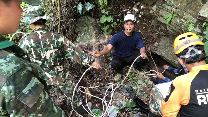 Expert mountaineering volunteers prepare to descend into an opening in the rock face to investigate if there is a route to the cave where the boys are. They are accompanied by National Park authority workers and Thai soldiers.