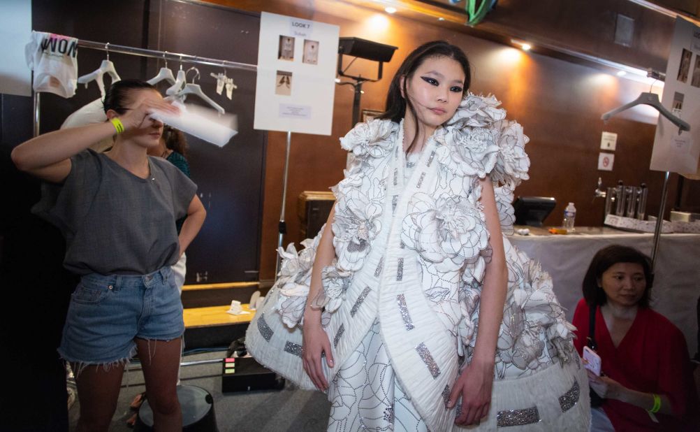 To help her beat the heat, an assistant fans an elaborately dressed model backstage. 