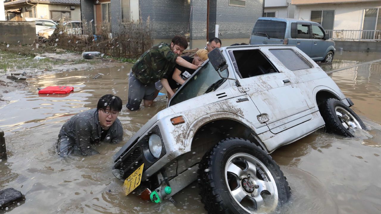 Residents try to upright a vehicle stuck in a flood hit area in Kurashiki, Okayama prefecture on July 9, 2018.