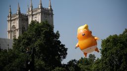 TOPSHOT - Pedestrians walk past as a giant balloon depicting US President Donald Trump as an orange baby floats next to the towers of Westminster Abbey during a demonstration against Trump's visit to the UK in Parliament Square in London on July 13, 2018. - US President Donald Trump launched an extraordinary attack on Prime Minister Theresa May's Brexit strategy, plunging the transatlantic "special relationship" to a new low as they prepared to meet Friday on the second day of his tumultuous trip to Britain. (Photo by Tolga AKMEN / AFP)        (Photo credit should read TOLGA AKMEN/AFP/Getty Images)