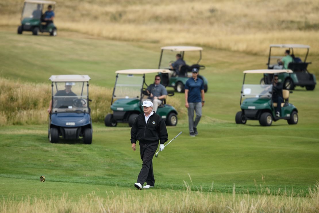 US President Donald Trump plays golf, wearing a hat with Trump and USA displayed on it.