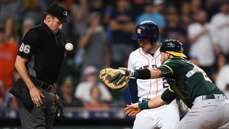 The baseball bounces off the chest of umpire David Rackley as Oakland Athletics catcher Jonathan Lucroy tries to tag out Houston Astros third baseman Alex Bregman at home plate during the eleventh inning in Houston on Tuesday, July 10.