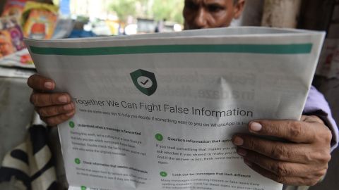 This photo illustration shows an Indian newspaper vendor reading a newspaper with a full back page advertisement from WhatsApp intended to counter fake information, in New Delhi on July 10, 2018.