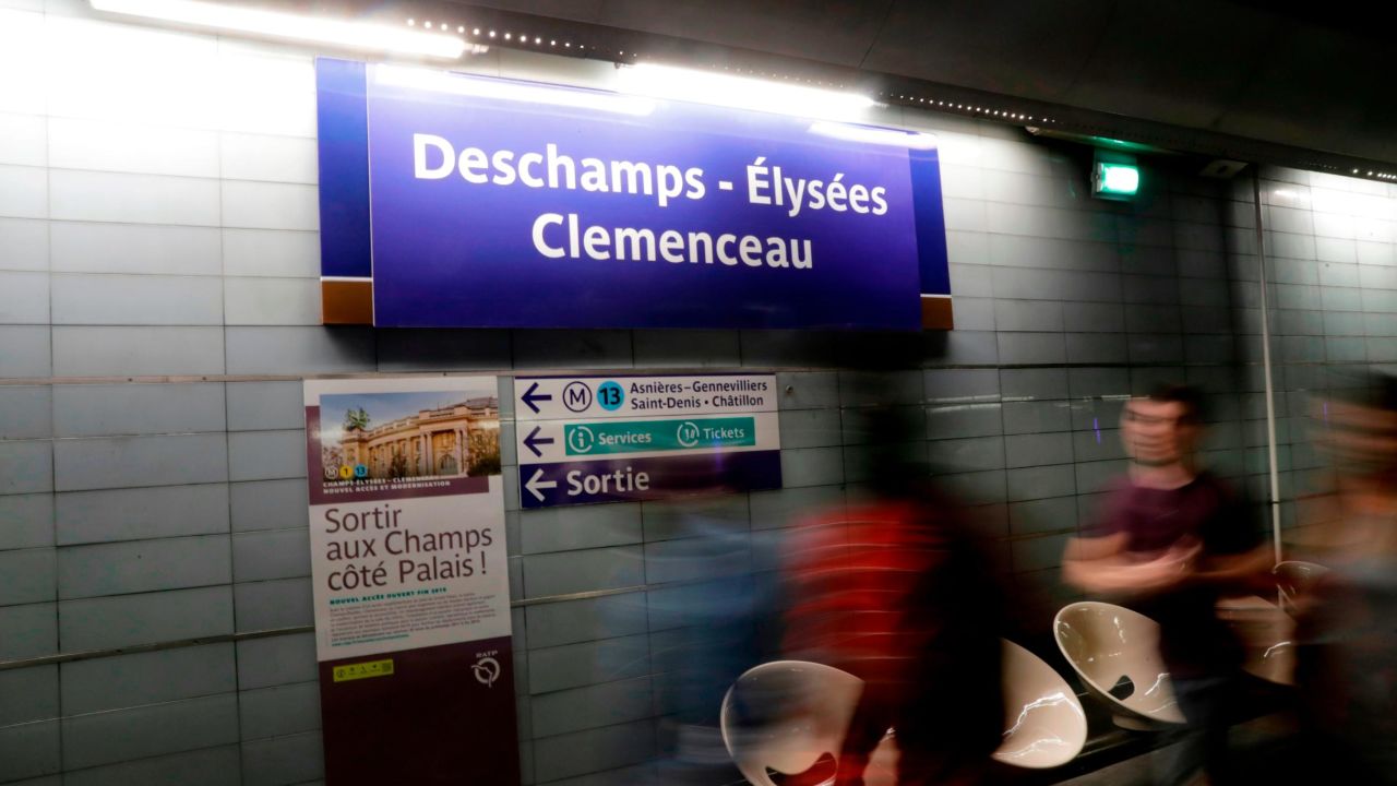 Commuters walk past a sign reading "Deschamps - Elysees Clemenceau." 