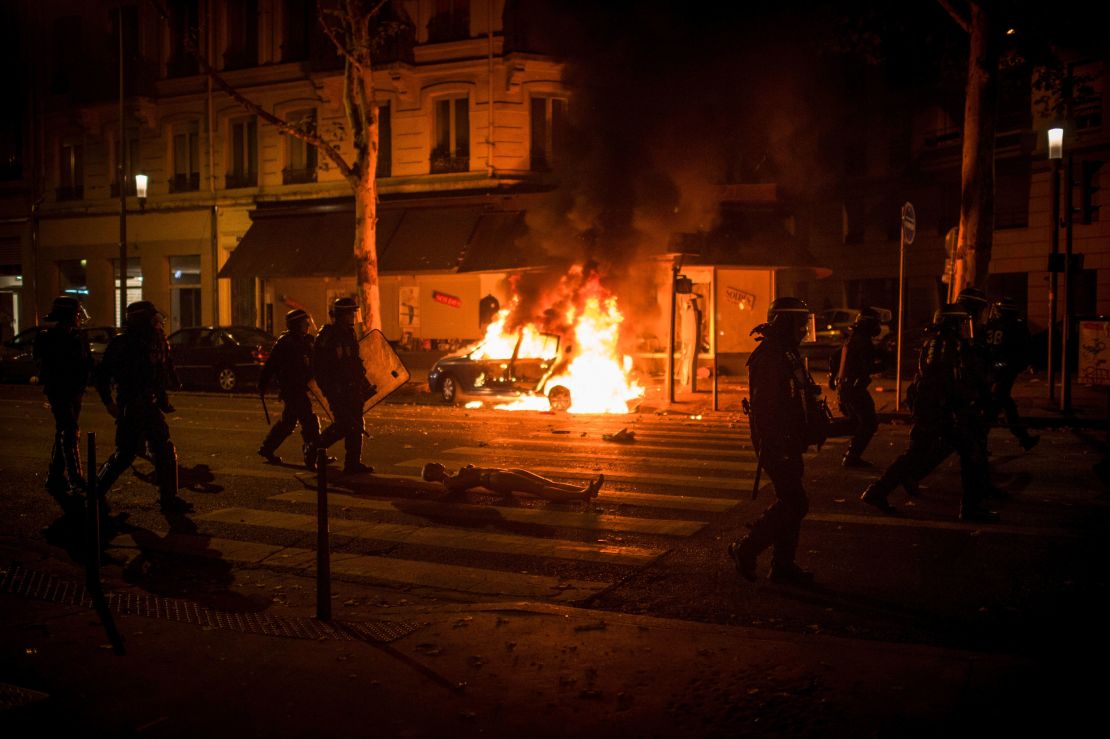 French anti-riot police officers walk by a burning car during clashes in Lyon on Sunday night. 