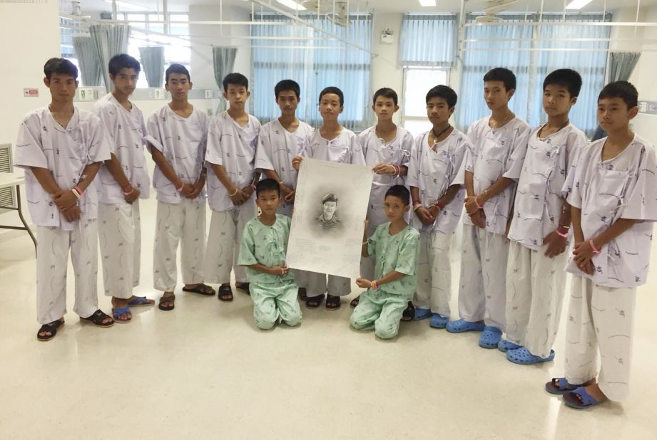 The team poses with a sketched portrait of Saman Kunan, a former Thai Navy SEAL who died on July 6 while returning from an operation to deliver oxygen tanks to the cave. He ran out of air while underwater, an official said.