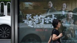 A woman walks past a poster of the film "Dying to Survive" at a bus stop in Beijing on July 12.
