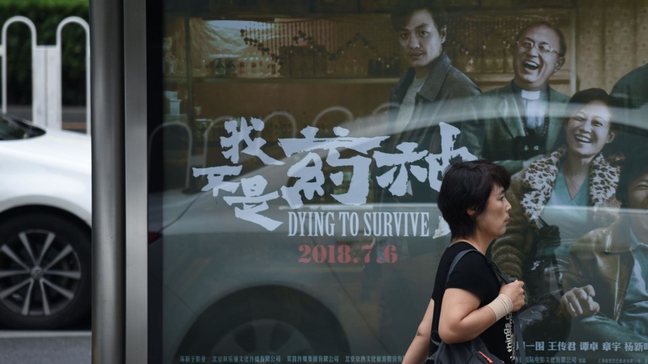 A woman walks past a poster of the film "Dying to Survive" at a bus stop in Beijing on July 12.