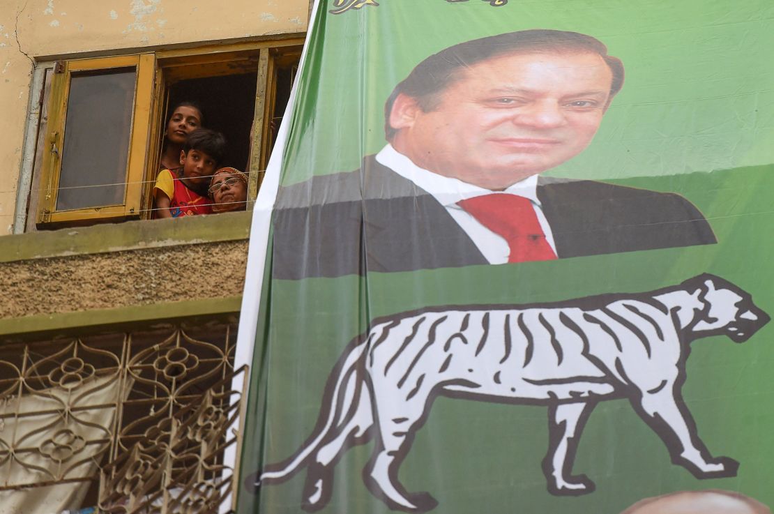 People look from a window next to an election banner featuring ousted prime minister Nawaz Sharif during a campaign event by his brother Shahbaz Sharif, head of Pakistan Muslim League -Nawaz (PML-N), in Karachi on June 26, 2018.