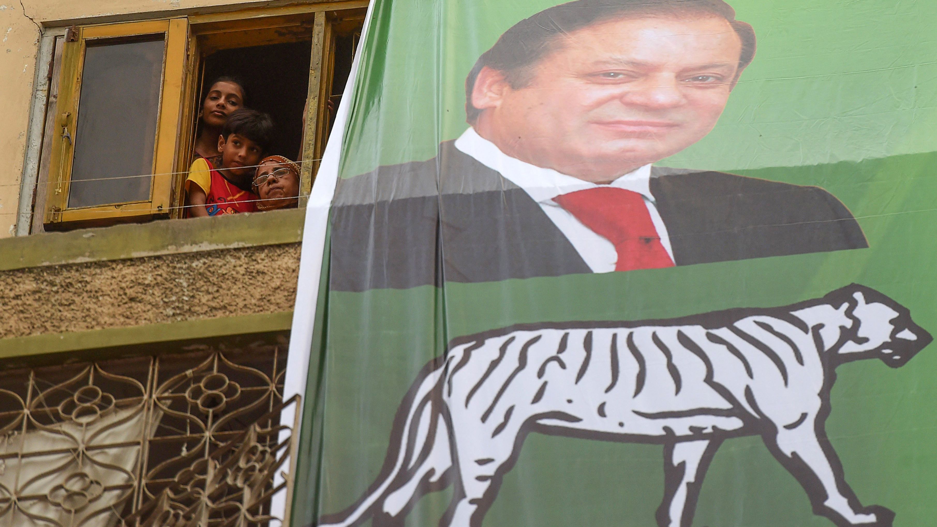 People look from a window next to an election banner featuring ousted prime minister Nawaz Sharif during a campaign event by his brother Shahbaz Sharif, head of Pakistan Muslim League -Nawaz (PML-N), in Karachi on June 26, 2018.