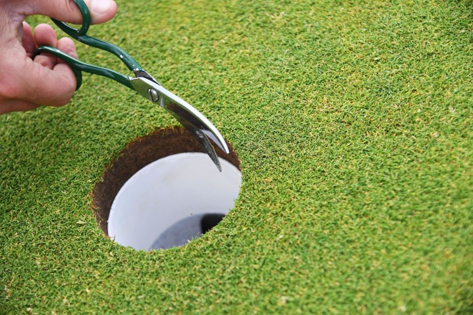 A greenskeeper trims the edges of a hole during the final round of the Open.