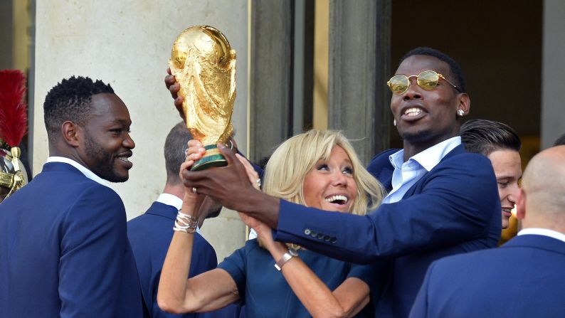 France's first lady, Brigitte Macron, lifts the World Cup trophy with help from Paul Pogba as the country's soccer team is received at the Elysee Palace in Paris on Monday, July 16.
