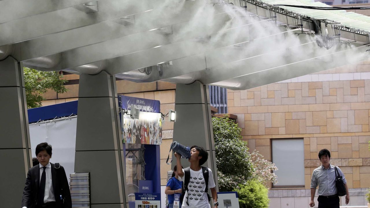 People cool down under the cooling mist spot in Tokyo, Monday, July 23, 2018. 