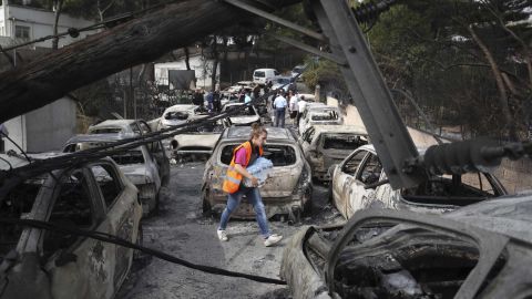A woman carries bottles of water as people stand amid the charred remains of burned-out cars in Mati east of Athens.