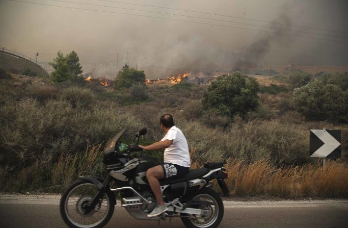 A motorcyclist passes burning brush on a road near Kineta.