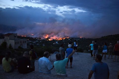 People watch as a wildfire takes hold in the town of Rafina on July 23.