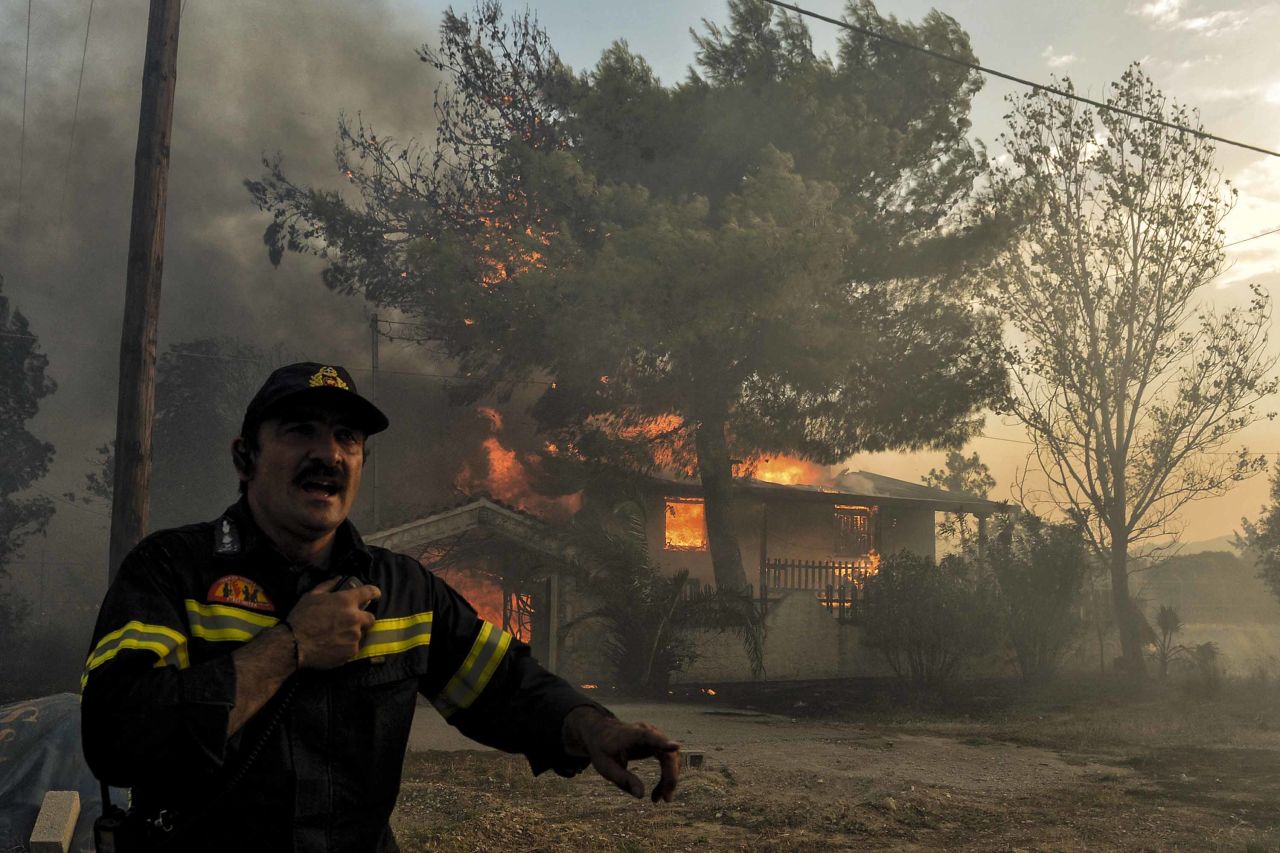 A firefighter reacts as a house burns in Kineta.