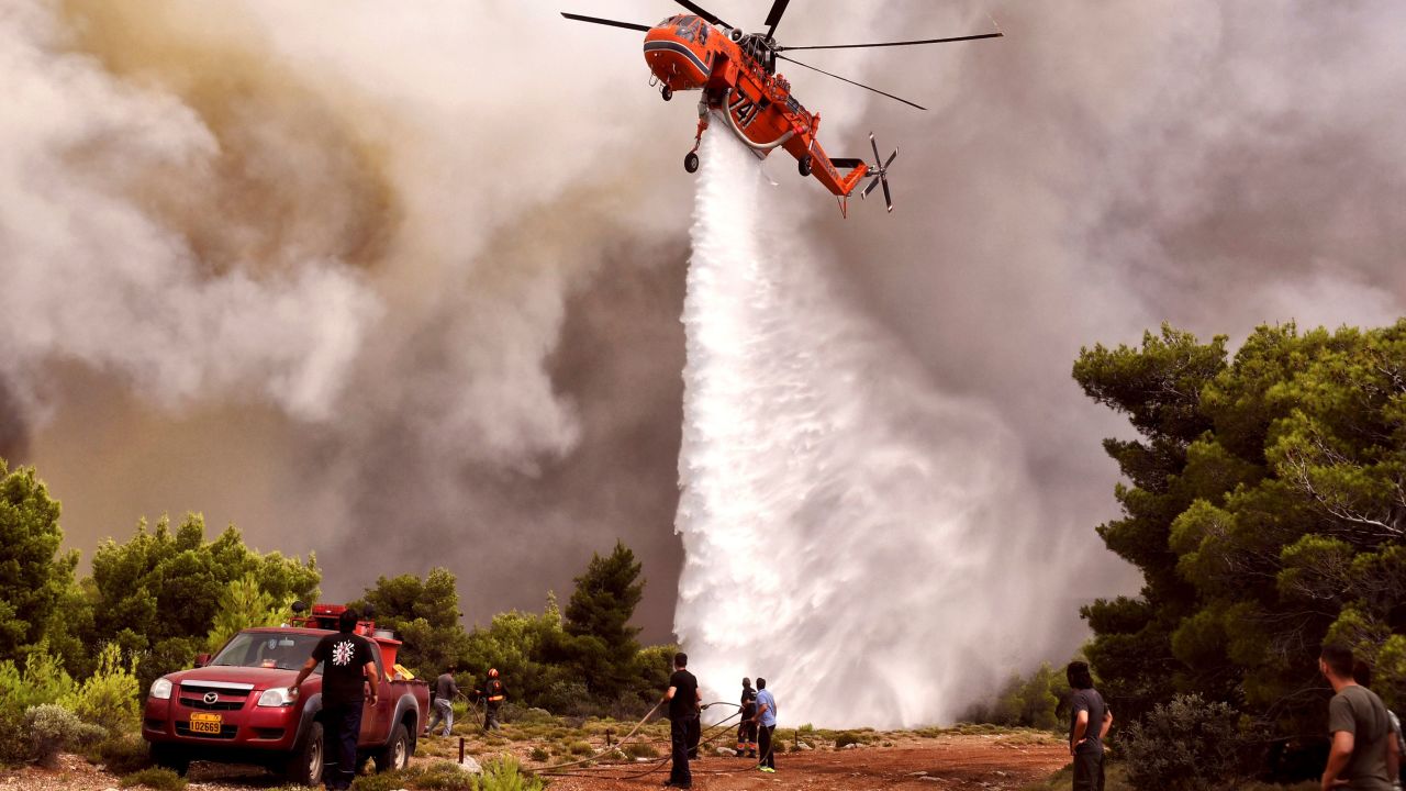 A firefighting helicopter drops water to extinguish flames Tuesday in the village of Kineta.