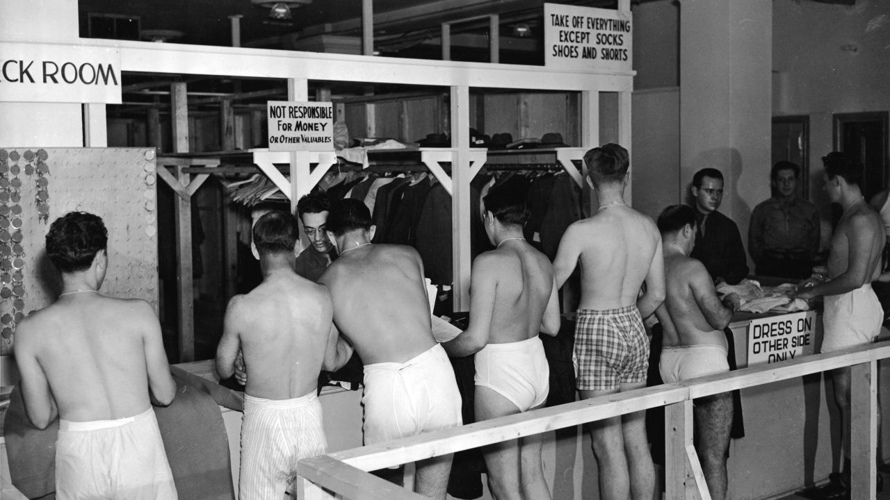 A line of underwear-clad draftees wait in line to check their clothes at an unidentified military facility in a 1944 photograph.