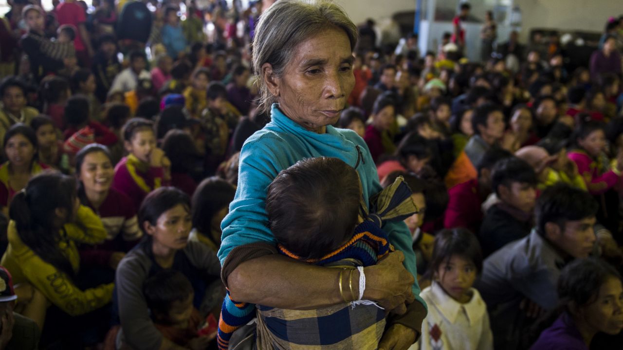 An elderly woman carries a child at a shelter.