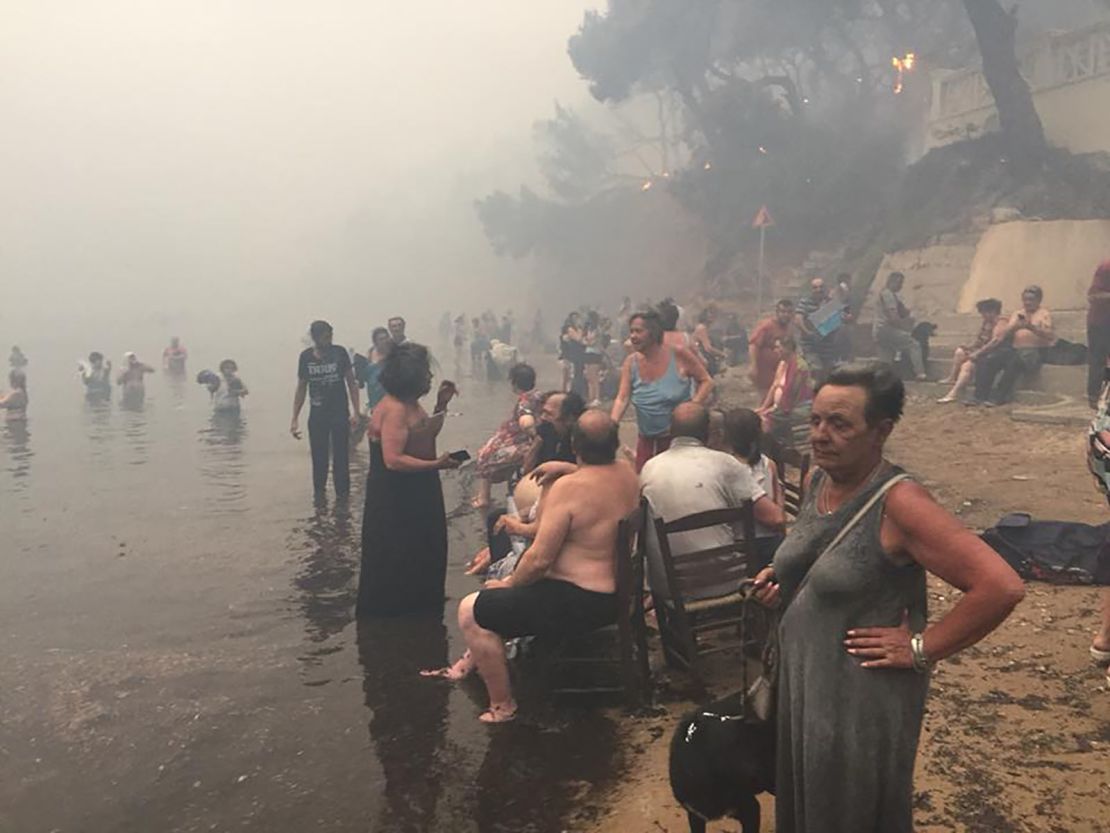 People take refuge Monday from the fires along the beach north of Mati.