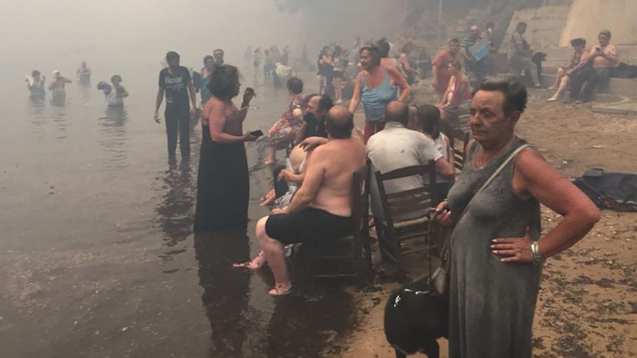 People take refuge Monday from the fires along the beach north of Mati.