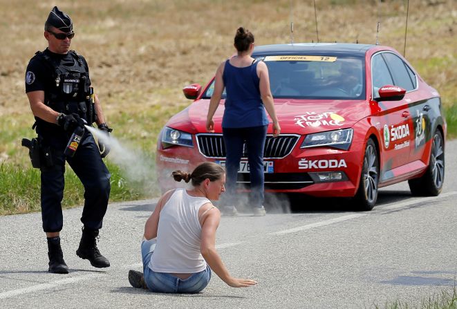A police officer sprays tear gas at one protester as another protester stands in front of the race director's car on July 24. Protesting farmers had blocked the road with hay bales, and <a href="index.php?page=&url=https%3A%2F%2Fwww.cnn.com%2F2018%2F07%2F24%2Fsport%2Ftour-de-france-protesters-pepper-spray%2Findex.html" target="_blank">the race was temporarily halted</a> after tear gas inadvertently got into the eyes of some riders.