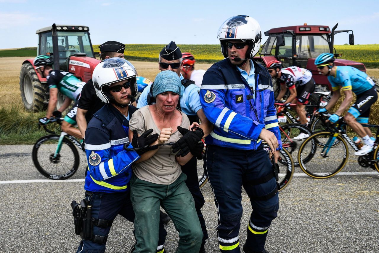 Gendarmes detain a protesting farmer as the pack rides behind them.