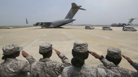 US service members salute as vehicles carry the remains.