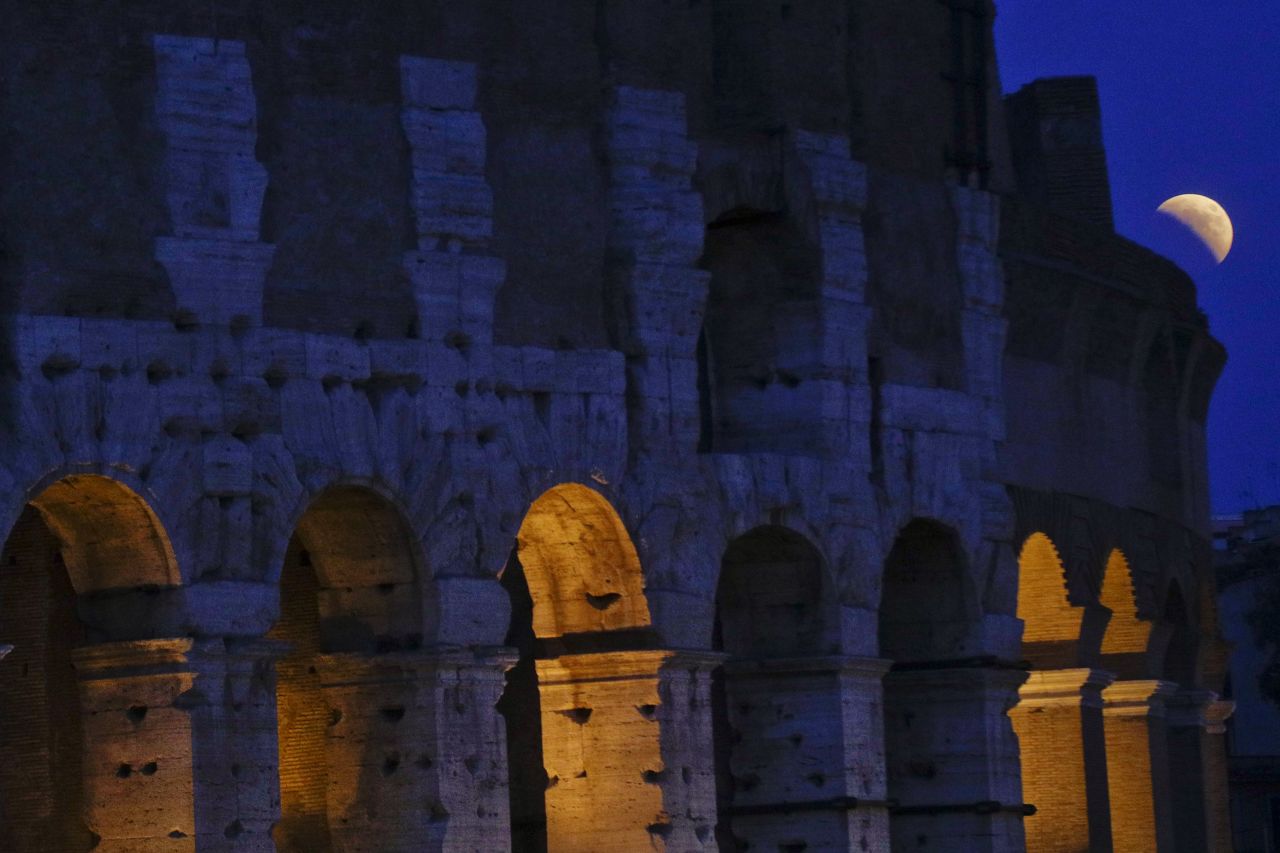 The moon peeks out next to the Colosseum in Rome.