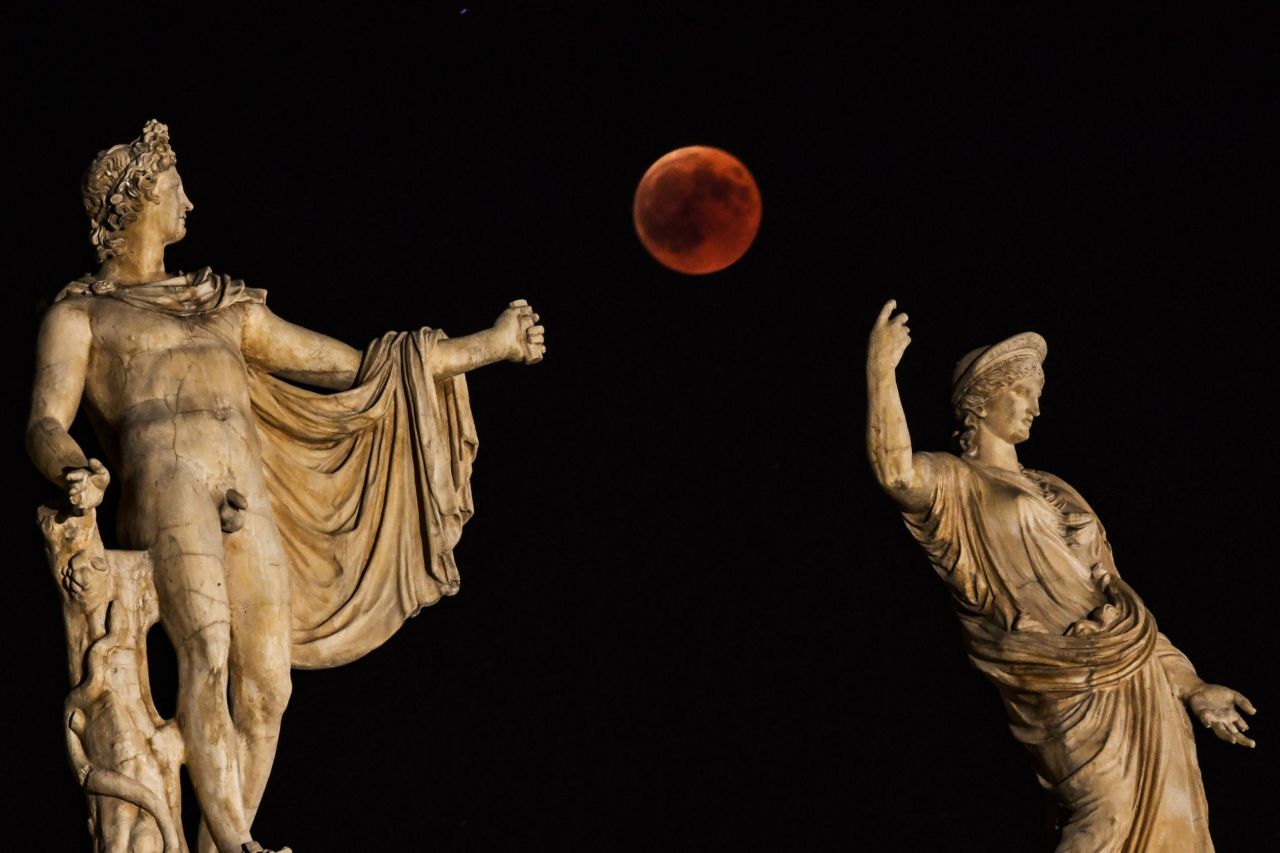 The blood moon is framed by the statues of Hera and Apollo in Athens, Greece.