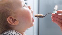 Mother feeds baby boy with a spoon porridge.