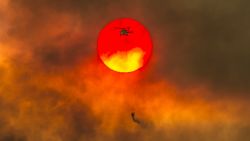 In this Friday, July 27, 2018 photo, a firefighting helicopter makes a water drop as the sun sets over a ridge burning near Redding, Calif., in efforts against the Carr Fire. Scorching heat, winds and dry conditions complicated firefighting efforts. (Hector Amezcua/The Sacramento Bee/ AP
