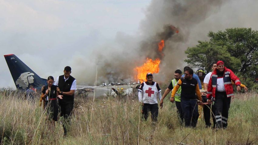 In this photo released by Red Cross Durango communications office, Red Cross workers and rescue workers carry an injured person on a stretcher, right, as airline workers, left, walk away from the site where an Aeromexico airliner crashed in a field near the airport in Durango, Mexico, Tuesday, July 31, 2018. The jetliner crashed while taking off during a severe storm, smacking down in a field nearly intact then catching fire, and officials said it appeared everyone on board escaped the flames. (Red Cross Durango via AP)