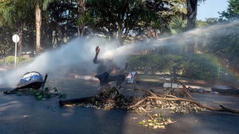 A protester is hit in the face with a water cannon Wednesday outside the gates of the Zimbabwe Electoral Commission in Harare.