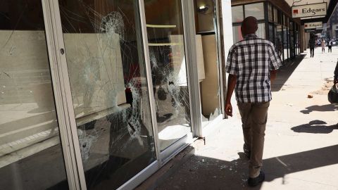 A man walks past smashed shop windows in Harare on Thursday.